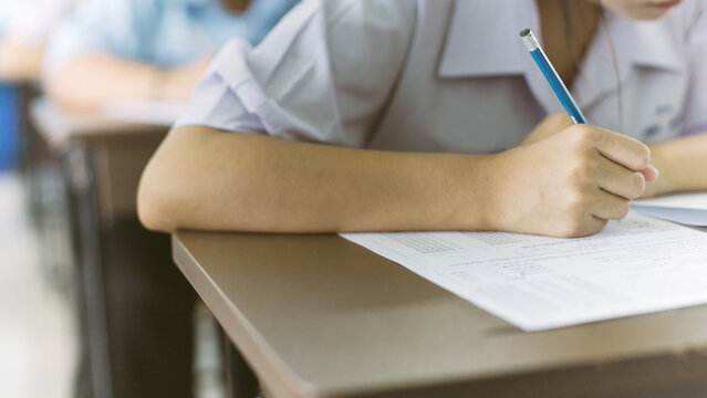 Close up hand of student reading and writing exam answer sheets exercises with stress in classroom