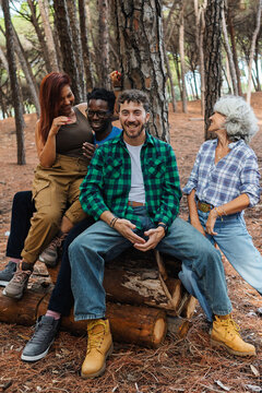 Smiling man in flannel shirt on stacked logs with friends in a forest