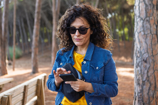 Middle aged woman in sunglasses using a smartphone in a pine forest
