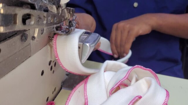 Close up of overlock sewing machine stitching cuff hem with pink thread.
garment factory worker sewing white fabric
