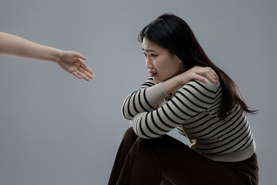Fearful woman sitting on ground protecting herself from helping hand