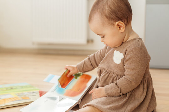 Baby turning pages of lift-the-flap book sitting on floor