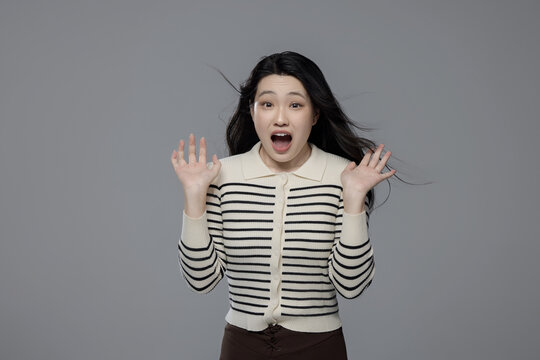 Surprised young Asian woman with open mouth and raised hands
