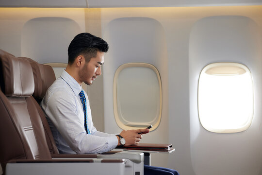 Young businessman using smartphone in airplane cabin