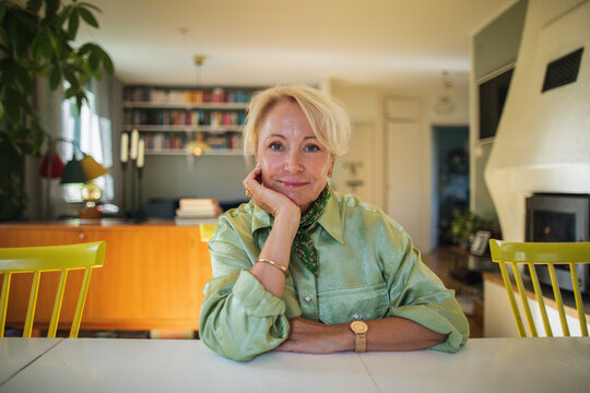 Portrait of senior blond woman leaning on elbow while sitting at table in home