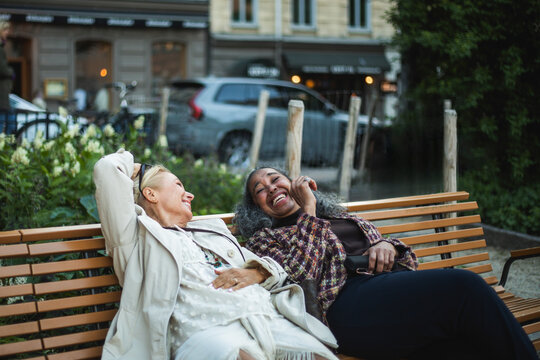Carefree mature woman enjoying leisure time leaning back on bench with female friend at park