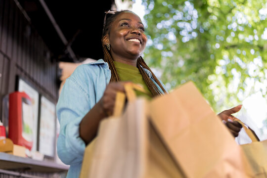 Low angle view of smiling woman walking with takeout food paper bags at street