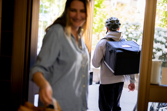 Rear view of delivery man carrying parcel bag leaving after giving home delivery