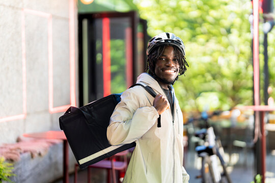 Portrait of smiling young male delivery worker carrying insulated bag standing at street