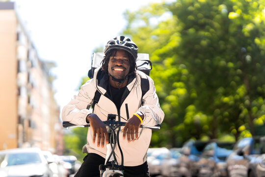 Portrait of happy young delivery man riding bicycle at street