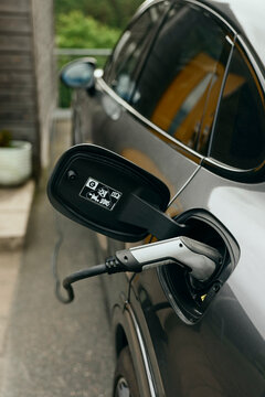 Cable connector plugged in open charging port of electric car stationed outside house in yard
