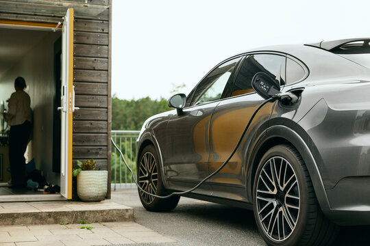 Electric car getting charged by cable connector in backyard of house