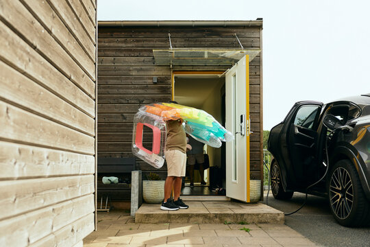 Boy carrying swimming float standing at front door of house while getting ready for weekend road trip