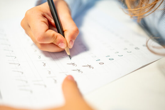 First grade student practices writing letters with pencil in workbook. Early literacy and handwriting skills develop with selective focus and shallow depth of field