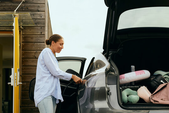 Woman charging electric car for road trip in backyard under sunny sky