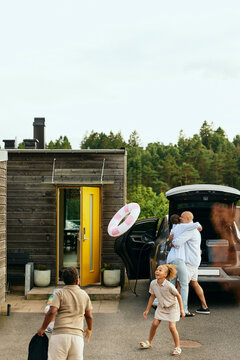 Children playing with swim ring while man embracing woman in background near car trunk