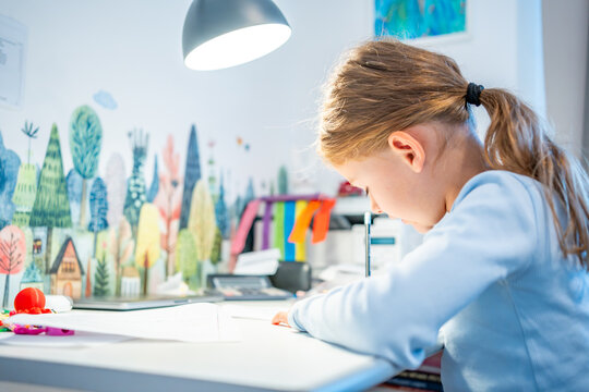 First grade girl practices handwriting at desk in her room. Child studies at home at beginning of school year with selective focus and soft background