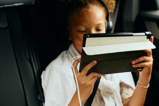 Girl watching video on tablet PC being charged while sitting in car during road trip