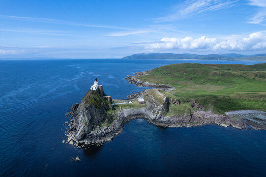 Aerial view of the Sanda Island lighthouse perched on a rocky cliff surrounded by the deep blue sea and green grassy hills in Argyll and Bute Council, Scotland, United Kingdom.