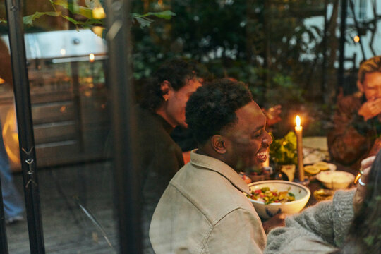 High angle view of happy young man sitting with friends at dinner in illuminated conservatory