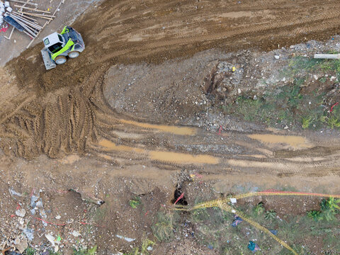 Aerial view of a skid-steer loader working on a muddy construction site with deep tire tracks and piles of earth in Istanbul, Istanbul, Turkiye.