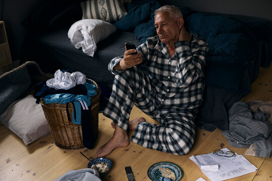 High angle view of lonely senior man using phone while sitting in messy bedroom