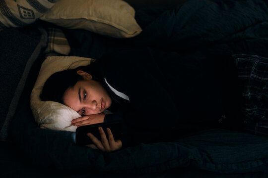 Teenage girl using smart phone while lying in bed before sleeping
