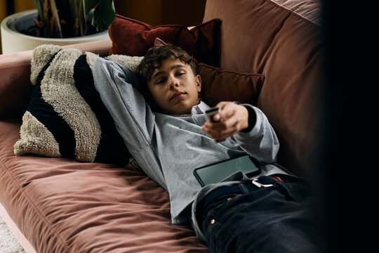 Teenage boy changing TV channels while lying on sofa at home