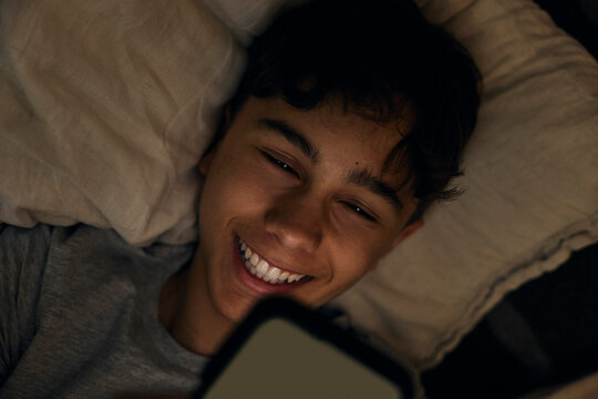 Directly above shot of happy teenage boy using phone while lying in bed