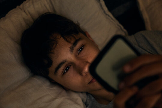 Directly above shot of teenage boy using mobile phone in bed at night