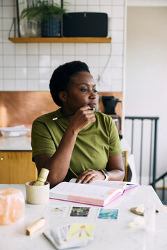 Thoughtful woman with hand on chin looking away while taking notes in book