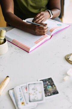 High angle view of woman writing in planner with tarot cards on table at home