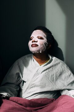 Woman doing her skincare routine while sitting against wall at home