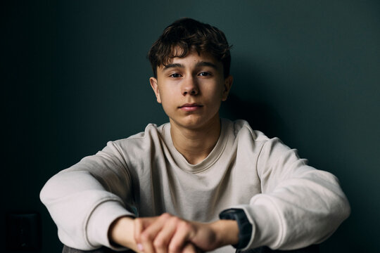 Portrait of teenage boy with blank expression sitting against wall