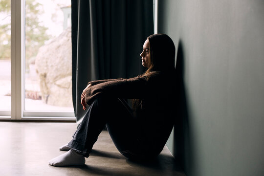 Side view of lonely teenage girl sitting by wall at home