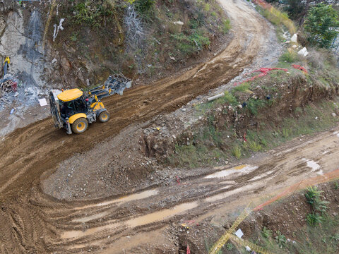 Aerial view of a yellow backhoe loader working on a muddy construction site with tire tracks and excavated earth in Istanbul, Istanbul, Turkiye.