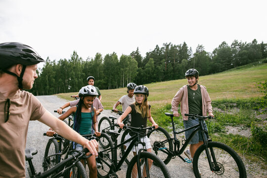 Children talking with camp counselor while wheeling mountain bikes on dirt path