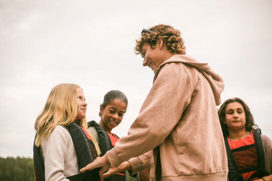 Smiling female counselor assisting girl in wearing life jacket during outdoor activity at summer camp