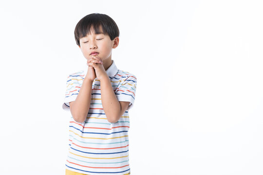 Young Boy with Hands Clasped in Prayer Against White Background