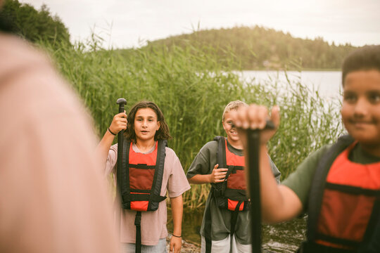 Boys wearing life jackets and holding oars while listening to camp leader before activity at summer camp