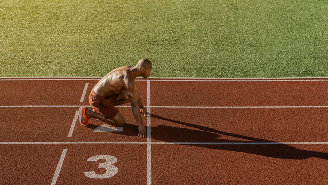Male athlete in starting position on athletics running track at stadium, sprint preparation, track and field training, competitive race, sports performance, fitness workout active lifestyle concept