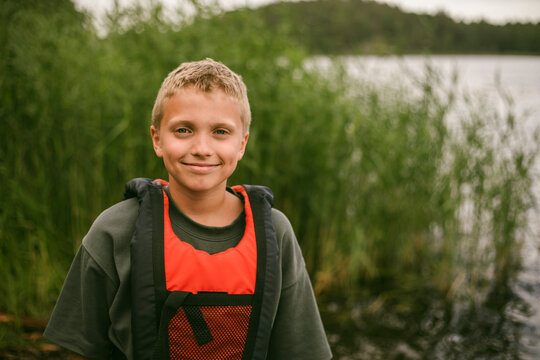 Portrait of smiling boy wearing life jacket by lake at summer camp