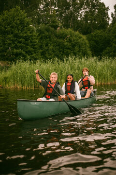 Happy kids canoeing with counselor during summer camp activity