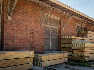 A weathered red brick historic warehouse exterior with a rustic wooden sliding door and stacked lumber bundles outside © Donald