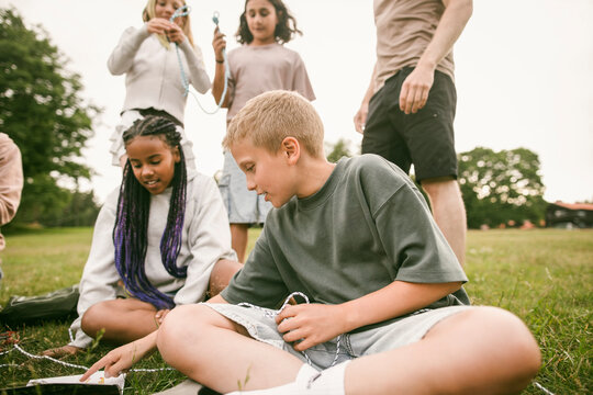 Boy and girl learning rope skills while sitting on grass at summer camp