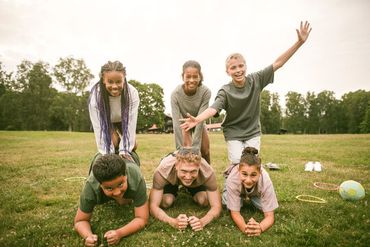 Group of happy children celebrating teamwork with counselor by stacking on top of each other after activity