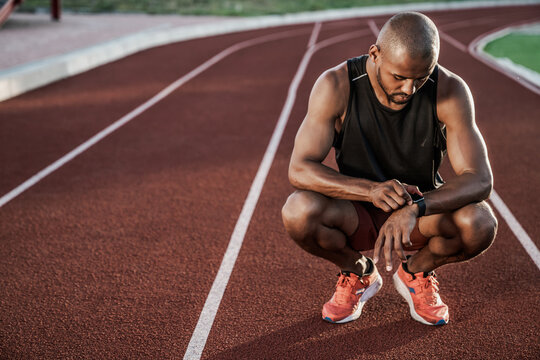 Young sportsman sitting on running track looking at smartwatch, fitness tracking, workout analysis, athlete recovery, sports technology, active lifestyle and outdoor training concept