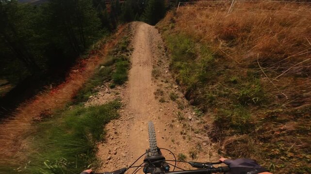 First-person POV footage of a mountain biker speeding downhill through a forest trail while following another cyclist, capturing fast movement, natural terrain and immersive outdoor action.