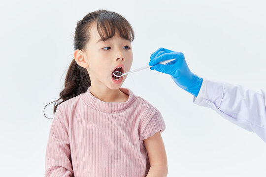 Doctor examining girl's throat with tongue depressor during medical checkup