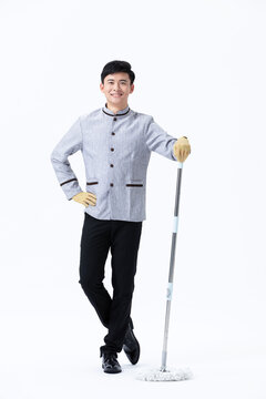 Happy young male cleaner in uniform holding a mop and wearing yellow gloves